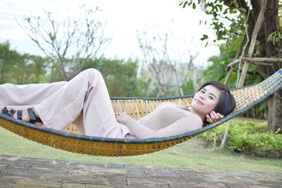 Woman lying down on hammock against trees