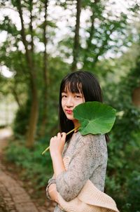 Portrait of young woman standing against tree