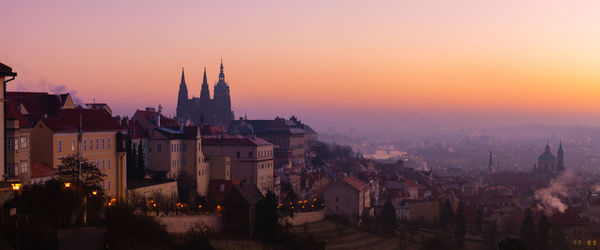 Illuminated buildings in city against sky during sunset