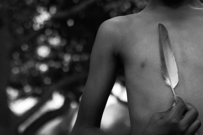 Midsection of shirtless boy holding feather