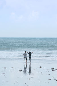 Rear view of couple standing on sea shore at beach against sky