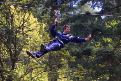 Low angle view of man zip lining at forest