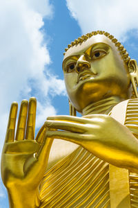 Low angle view of golden buddha statue against sky