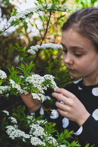 Young girl admiring tiny white spring flowers known as bridal wreath. blooming spiraea in garden.