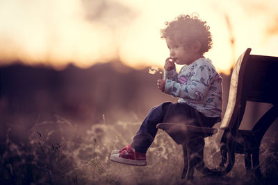 Side view of girl sitting on bench at park during sunset