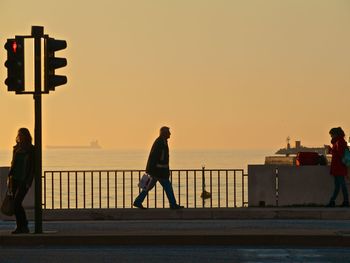 People on railing against sea during sunset