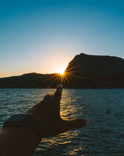 Cropped hand against sea during sunset