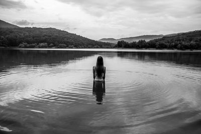 Rear view of woman standing in lake against sky