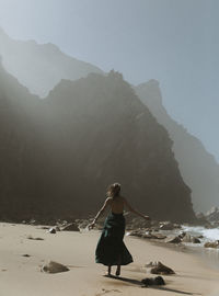 Rear view of woman standing on beach against sky