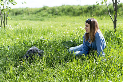 Pretty young woman resting with fluffy dog on green grass in summer, pet love and care, walking dog