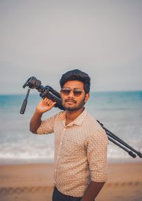 Young man holding camera while standing on beach