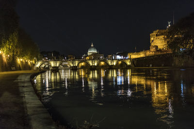 Illuminated bridge over river against buildings at night