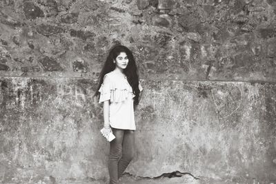 Portrait of young woman standing against wall