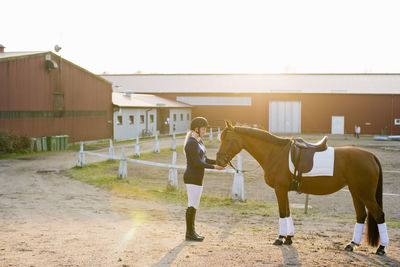 Teenage girl with horse standing against barn