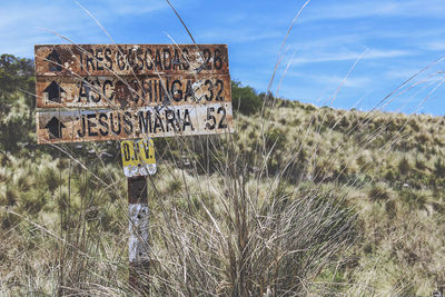 Close-up of information sign on field against sky