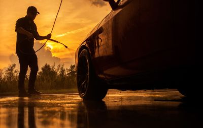 Low angle view of man washing car against sky during sunset