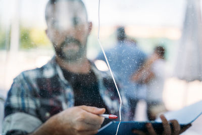 Reflection of man photographing through mobile phone on window