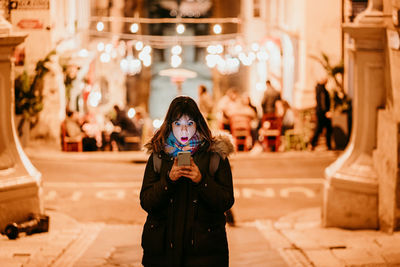 Portrait of woman standing against illuminated wall during winter