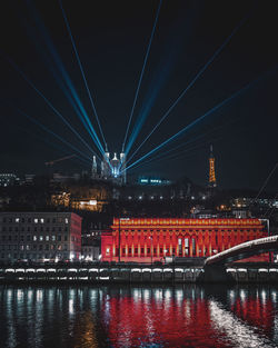 Illuminated bridge over river by buildings against sky at night