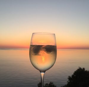 Close-up of wineglass against sky during sunset