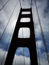 Low angle view of suspension bridge against cloudy sky