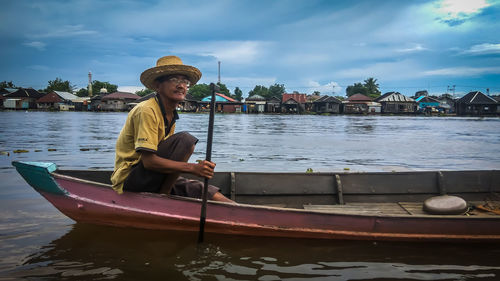 Portrait of man with boat on river against sky