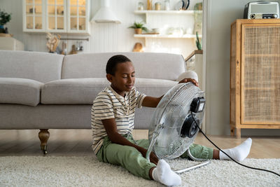 African american boy child suffering from heat sitting in front of electric fan at home