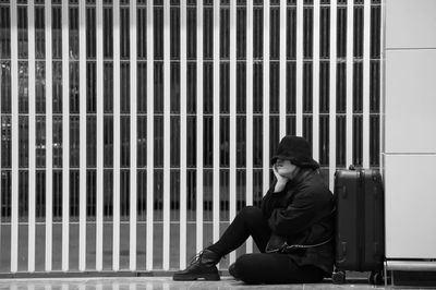 Side view of woman sitting on footpath by luggage