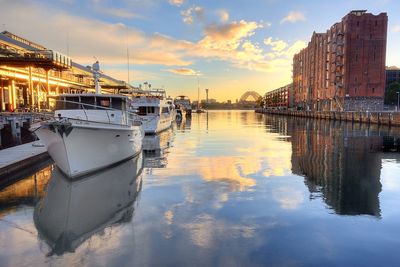 Boats moored at harbor by building against sky during sunset