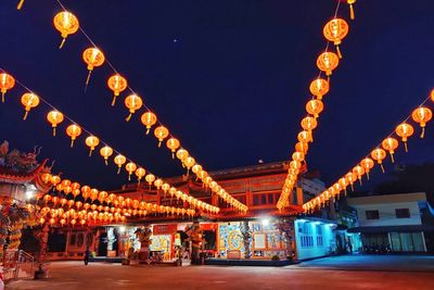 Illuminated lanterns hanging by building against sky at night