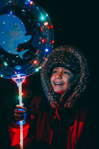 Smiling boy holding illuminated balloon at night during winter