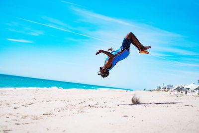 People jumping on beach against blue sky