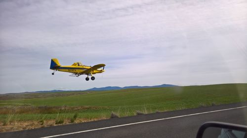 Airplane flying over road against sky