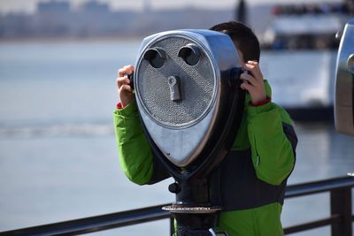 Boy looking through coin-operated binoculars against river