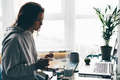 Side view of young woman using mobile phone at home