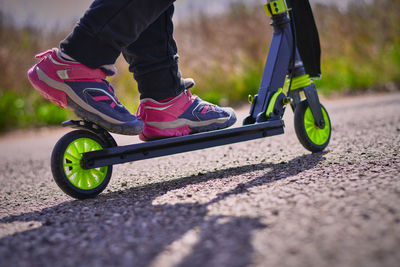 Low section of man riding push scooter on road