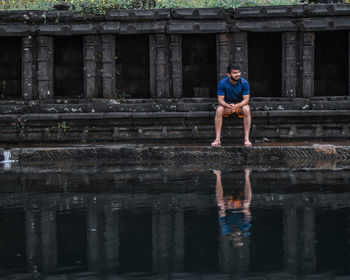 Man looking away while sitting on staircase by lake