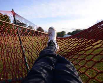 Low section of man relaxing on hammock in park against sky
