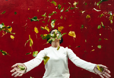 Woman throwing leaves while standing against wall