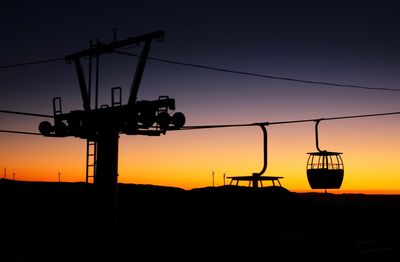 Silhouette cranes on land against sky during sunset