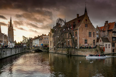 View of buildings by river against cloudy sky