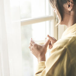 Woman drinking a cup of tea looking outside the window portrait of a girl enjoying free time at home