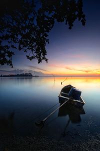 Boat moored on lake against sky at sunset