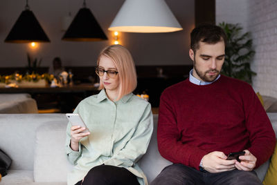 Man and woman using phone while sitting at home