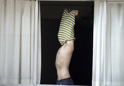 Midsection of woman standing by window at home