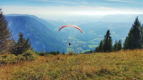 Person paragliding over mountains against blue sky