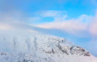 Snow covered mountain peaks disappear into white clouds under a clear blue sky in the morning light