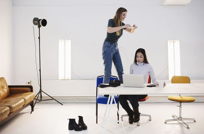 Blogger photographing colleague using laptop at desk in office