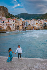 People on sea by city against sky