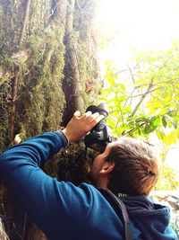 Portrait of boy photographing with mobile phone while standing on tree